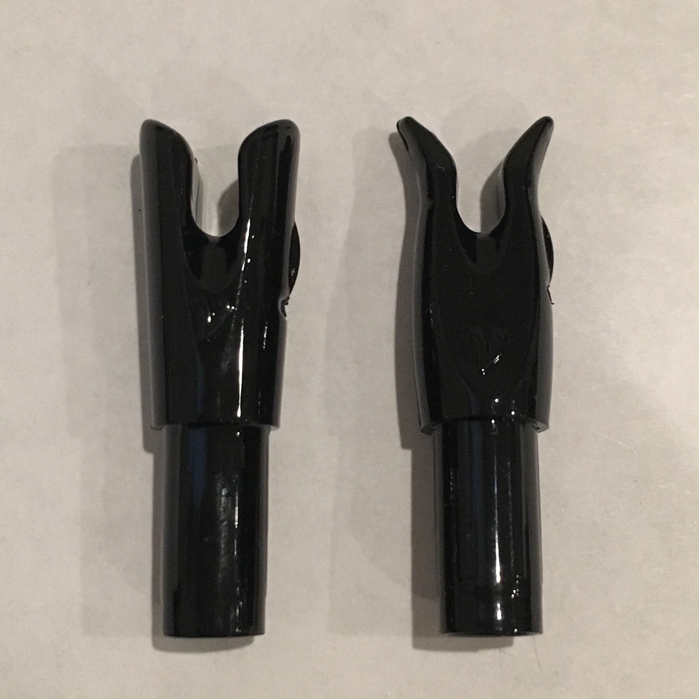 Two black Vermil arrow nocks standing upright, photographed close on a pale background.