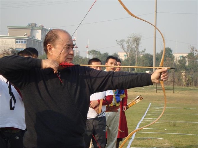An archer at full draw with a Mariner laminated bow on an outdoor practice field.